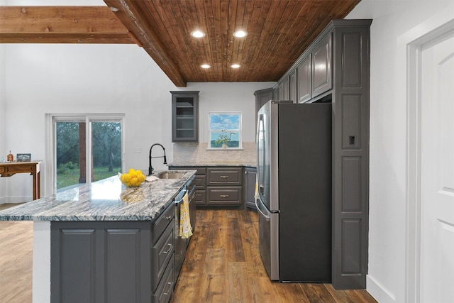 kitchen featuring gray cabinetry, backsplash, a kitchen island with sink, appliances with stainless steel finishes, and light stone counters