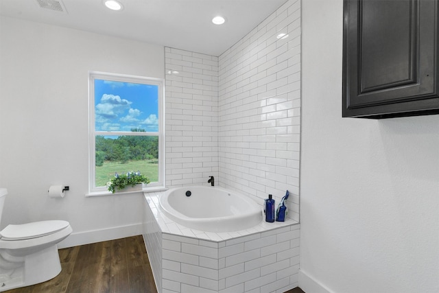 bathroom with tiled tub, wood-type flooring, and toilet