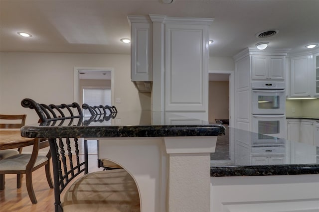 kitchen with a peninsula, double oven, white cabinets, and dark stone countertops