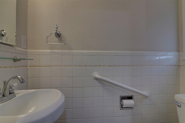 bathroom with wainscoting, a sink, toilet, and tile walls