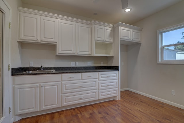 kitchen with dark stone counters, hardwood / wood-style floors, sink, and white cabinets