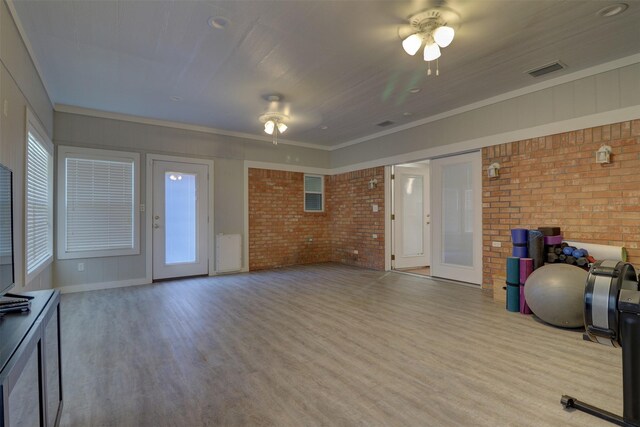 exercise area with light hardwood / wood-style flooring, ceiling fan, brick wall, and ornamental molding