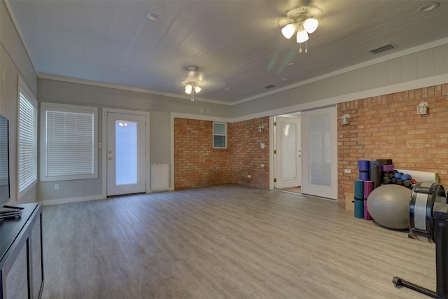 exercise room with brick wall, light wood-style flooring, and visible vents