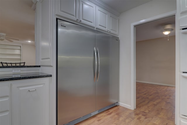 kitchen with light hardwood / wood-style flooring, stainless steel built in fridge, white cabinetry, and dark stone counters