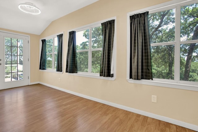 spare room featuring plenty of natural light, wood-type flooring, and vaulted ceiling