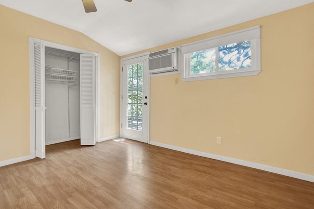 unfurnished bedroom with ceiling fan, vaulted ceiling, an AC wall unit, and light hardwood / wood-style flooring