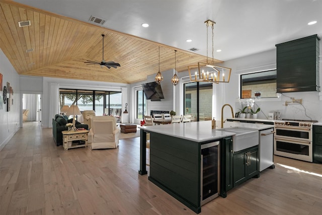 kitchen featuring wood ceiling, appliances with stainless steel finishes, a center island with sink, decorative light fixtures, and beverage cooler