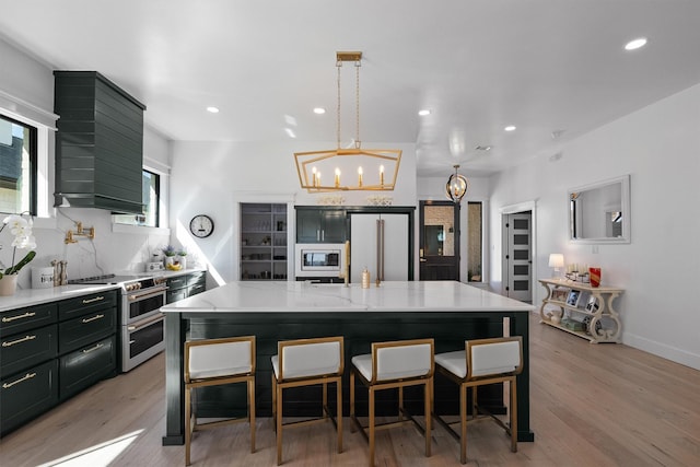 kitchen with light stone counters, double oven range, decorative light fixtures, and a large island with sink