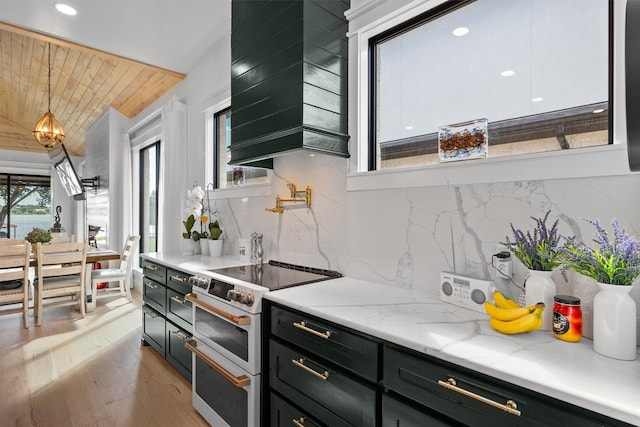 kitchen with custom exhaust hood, tasteful backsplash, hanging light fixtures, light stone countertops, and range with two ovens