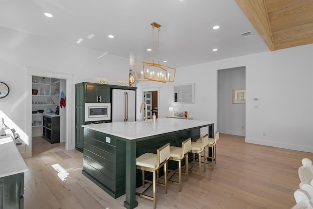 kitchen featuring high end fridge, hanging light fixtures, light stone counters, built in microwave, and a large island with sink