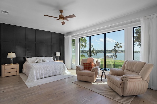 bedroom featuring multiple windows, light hardwood / wood-style flooring, ceiling fan, and a water view