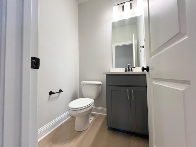 half bath with toilet, wood finished floors, baseboards, and vanity