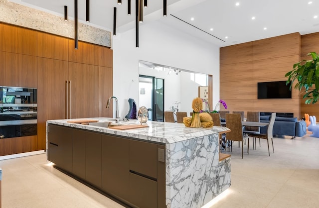 kitchen featuring wooden walls, sink, a high ceiling, and a center island with sink