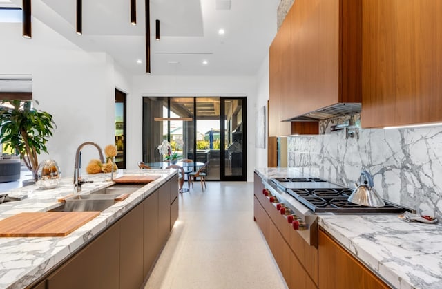 kitchen with backsplash, light stone counters, stainless steel gas cooktop, sink, and range hood