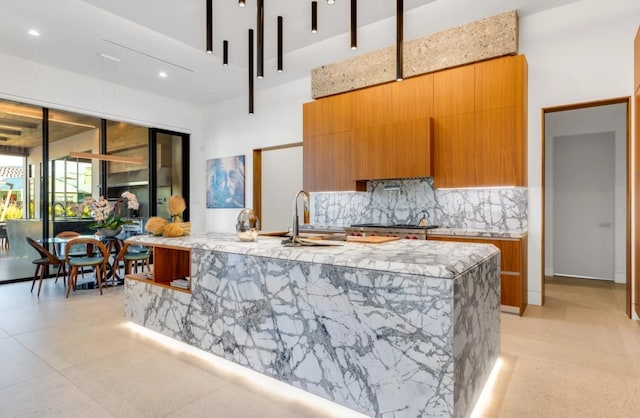 kitchen with a high ceiling, sink, a center island with sink, and backsplash