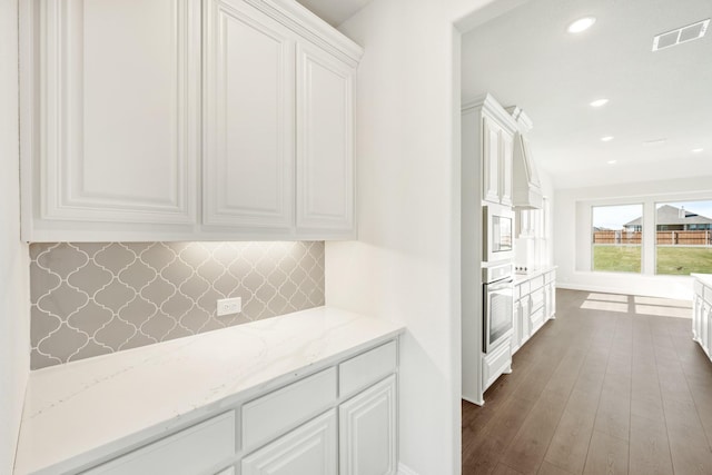 kitchen featuring white cabinetry, dark hardwood / wood-style floors, tasteful backsplash, light stone countertops, and oven