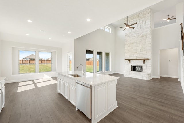 kitchen with a stone fireplace, dishwasher, sink, white cabinets, and a center island with sink