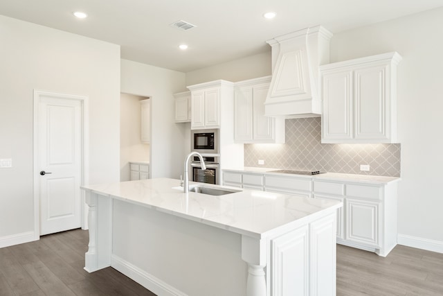 kitchen featuring premium range hood, sink, black appliances, a center island with sink, and white cabinets