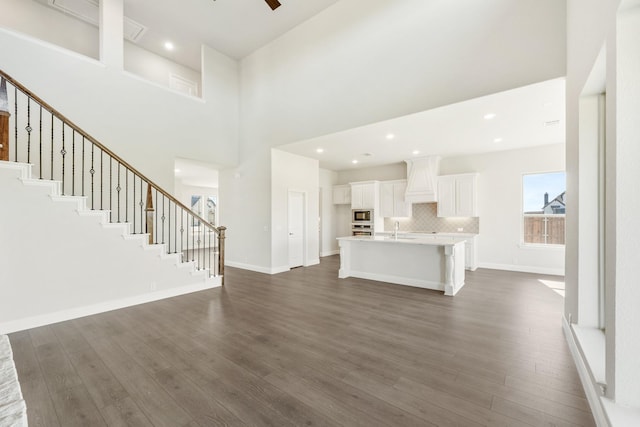 unfurnished living room with dark hardwood / wood-style flooring, sink, a towering ceiling, and ceiling fan