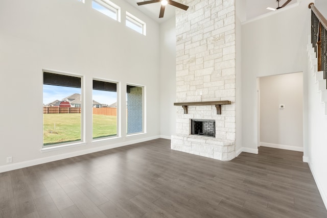 unfurnished living room featuring a high ceiling, ceiling fan, dark hardwood / wood-style flooring, and a fireplace