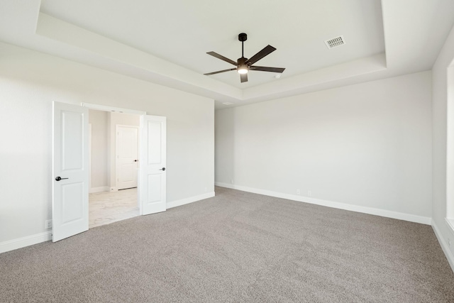 spare room featuring ceiling fan, light colored carpet, and a tray ceiling