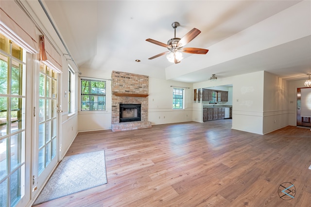 unfurnished living room featuring ceiling fan, light hardwood / wood-style flooring, a wealth of natural light, and a brick fireplace