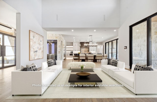 living room featuring plenty of natural light, a chandelier, a high ceiling, and light wood-type flooring