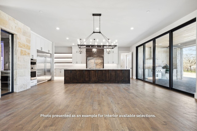 kitchen with a center island with sink, decorative light fixtures, built in refrigerator, dark brown cabinets, and white cabinetry