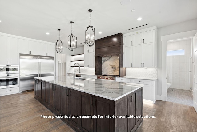 kitchen featuring appliances with stainless steel finishes, custom exhaust hood, dark brown cabinetry, a spacious island, and sink