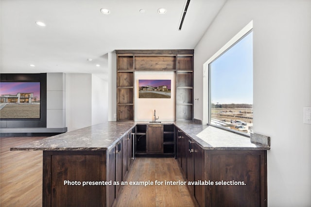 bar featuring dark brown cabinetry, stone counters, and light hardwood / wood-style floors