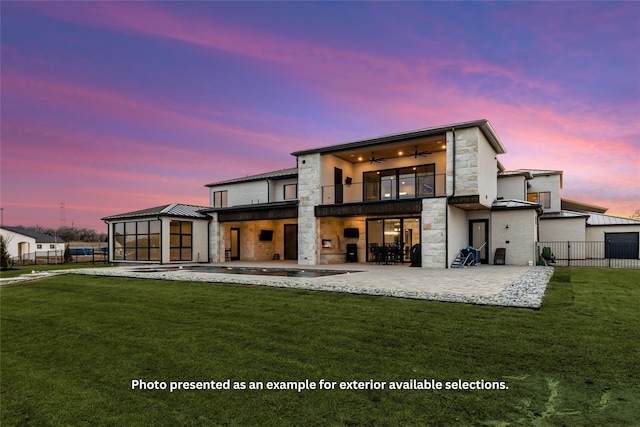 back house at dusk featuring a yard, a balcony, a patio, and ceiling fan