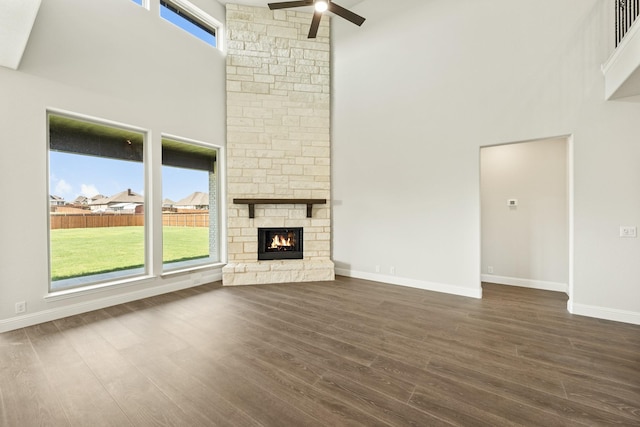 unfurnished living room featuring a towering ceiling, baseboards, a stone fireplace, ceiling fan, and dark wood-type flooring