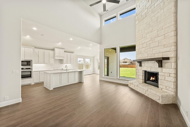 unfurnished living room featuring a sink, baseboards, ceiling fan, and dark wood-style floors