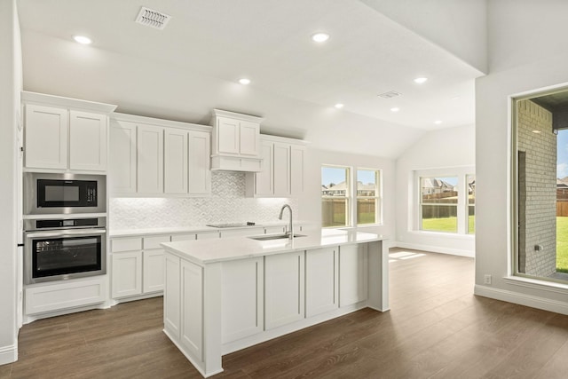 kitchen with light countertops, tasteful backsplash, a sink, black appliances, and vaulted ceiling