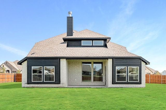 rear view of property with a chimney, roof with shingles, brick siding, a fenced backyard, and a yard