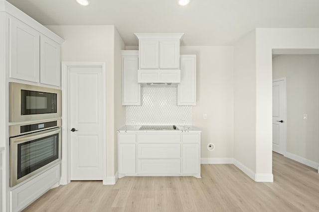 kitchen featuring backsplash, light countertops, baseboards, black appliances, and light wood-style floors