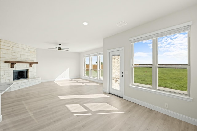 unfurnished living room featuring a ceiling fan, a stone fireplace, visible vents, baseboards, and light wood finished floors