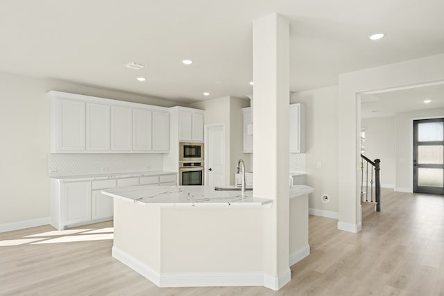 kitchen with white cabinets, stainless steel appliances, light wood-type flooring, and tasteful backsplash