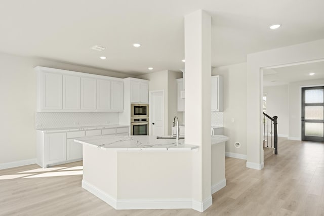 kitchen with backsplash, appliances with stainless steel finishes, light wood-type flooring, a sink, and white cabinets