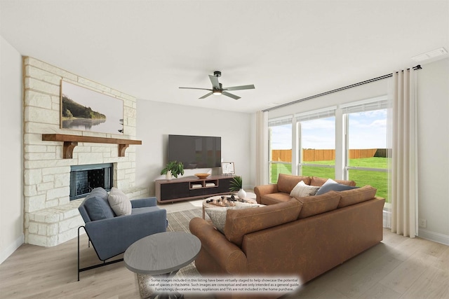 living area with baseboards, ceiling fan, a stone fireplace, and light wood-style flooring
