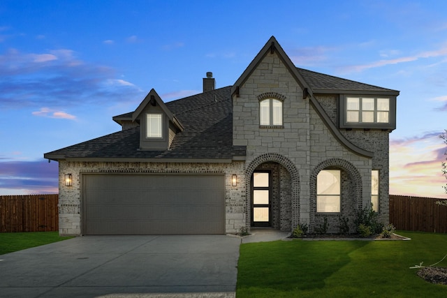 french country home featuring fence, driveway, stone siding, an attached garage, and a yard