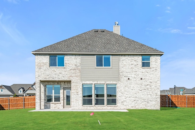 back of property with a fenced backyard, a chimney, a shingled roof, a patio area, and a lawn