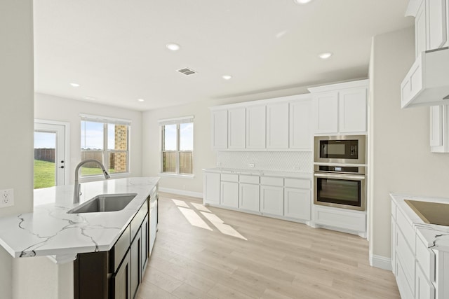 kitchen featuring built in microwave, a sink, light stone counters, light wood finished floors, and oven