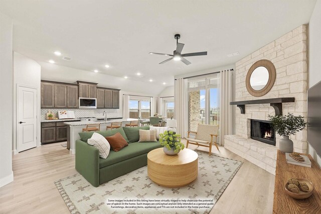 living room featuring a stone fireplace, lofted ceiling, sink, ceiling fan, and light hardwood / wood-style flooring