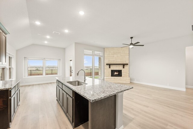 kitchen featuring light stone countertops, an island with sink, a stone fireplace, and sink