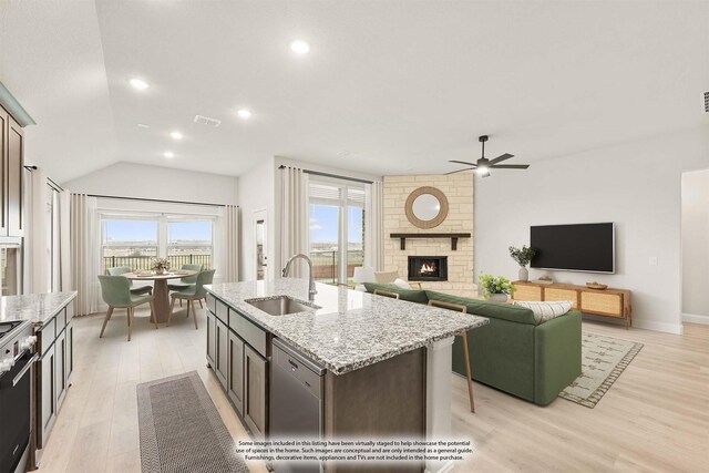 kitchen with sink, an island with sink, stainless steel appliances, a fireplace, and light stone countertops