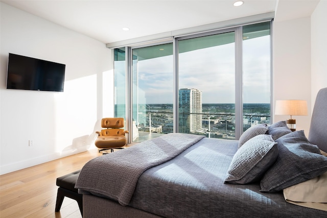 bedroom with multiple windows, a wall of windows, access to outside, and hardwood / wood-style flooring