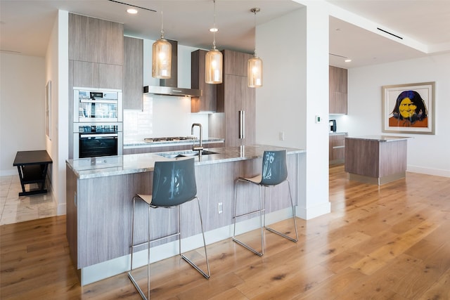 kitchen featuring light stone countertops, a kitchen breakfast bar, backsplash, wall chimney exhaust hood, and decorative light fixtures