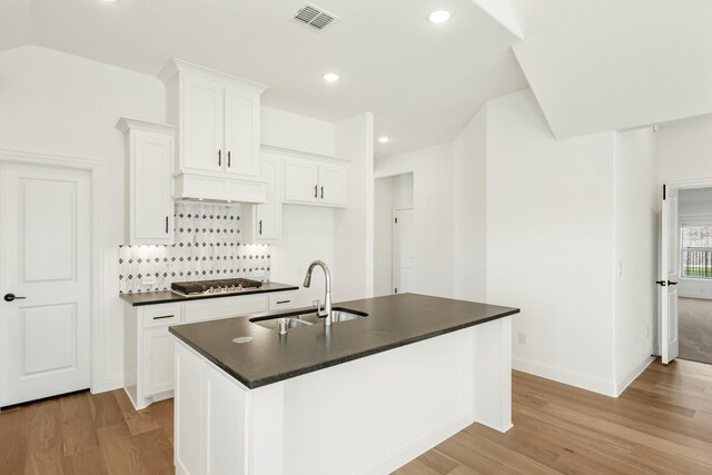 kitchen with custom exhaust hood, a kitchen island with sink, sink, white cabinetry, and stainless steel gas stovetop