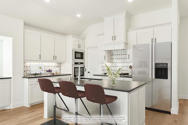 kitchen with white cabinetry, stainless steel appliances, vaulted ceiling, a breakfast bar area, and a center island with sink